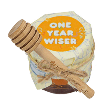 Honey container with wooden dipper labeled 'One Year Wiser' on a white background
