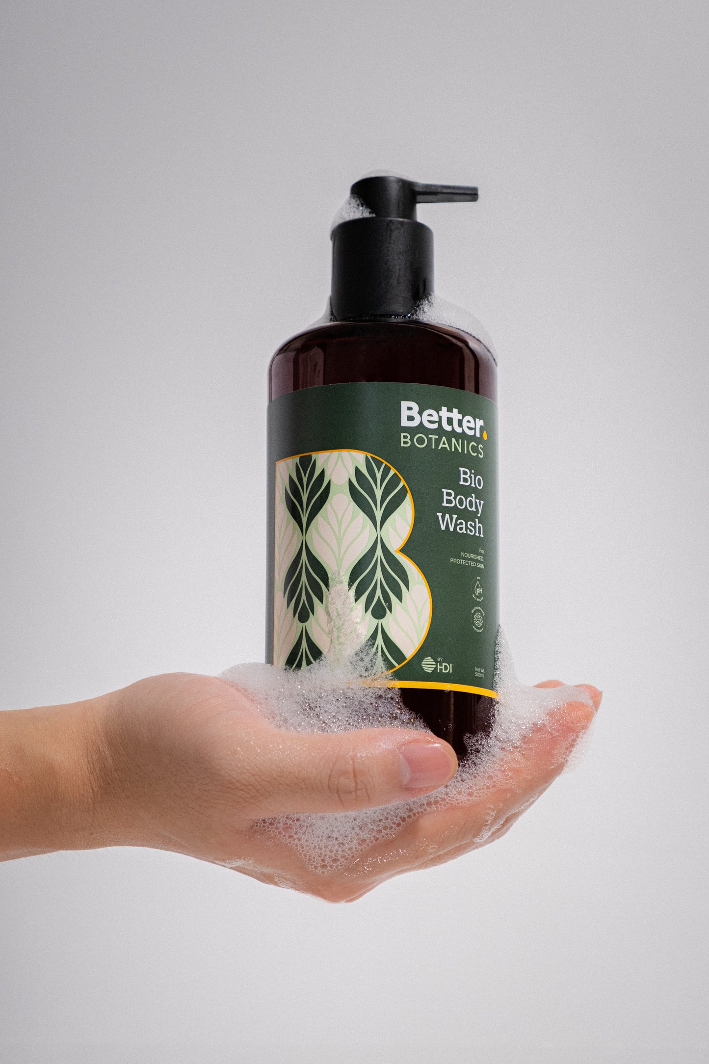 Hand holding a bottle of Better Botanics body wash with a white background