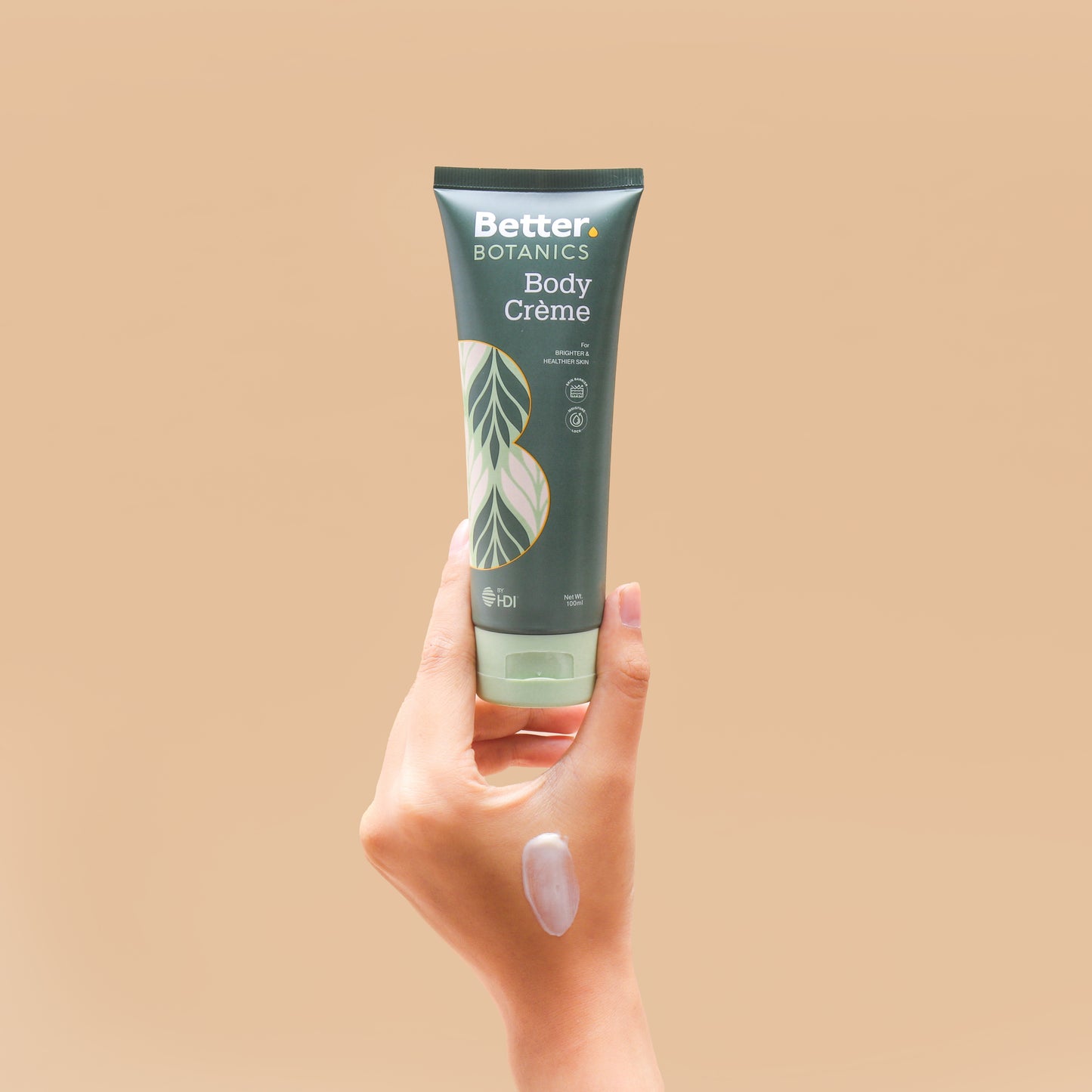 Hand holding a tube of Better Botanics Body Creme against a beige background