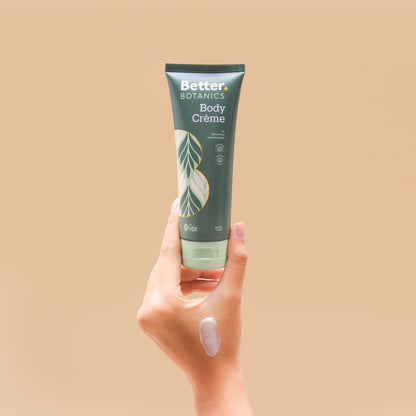 Hand holding a tube of Better Botanics Body Creme against a beige background