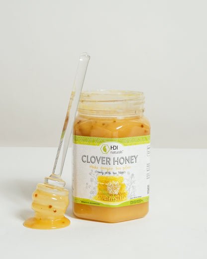 Jar of clover honey with a honey dipper on a white background