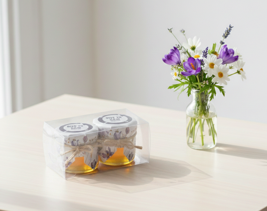 Two jars of honey with a small bouquet of flowers on a light surface.