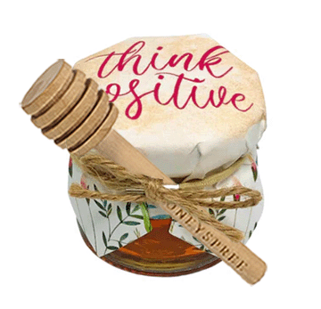 Jar of honey with a wooden dipper and 'think positive' lid on a white background