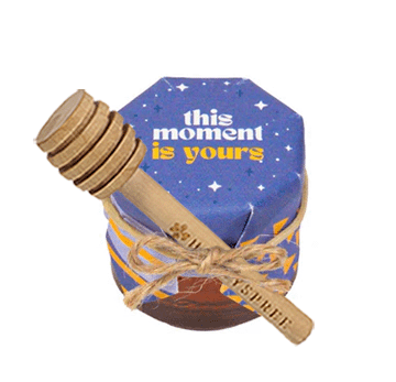 Decorative jar with wooden spoon and 'this moment is yours' text on a white background