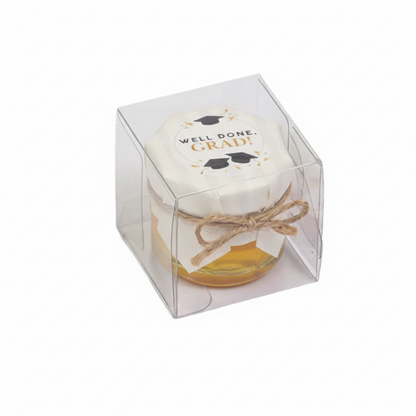 Jar of honey with a decorative label in a clear cube packaging on a white background