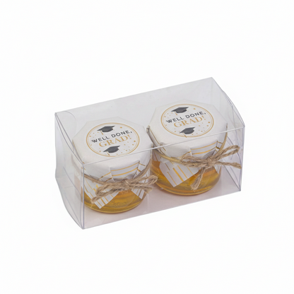 Two small jars with 'Well Done Grad' labels in a clear packaging box on a white background
